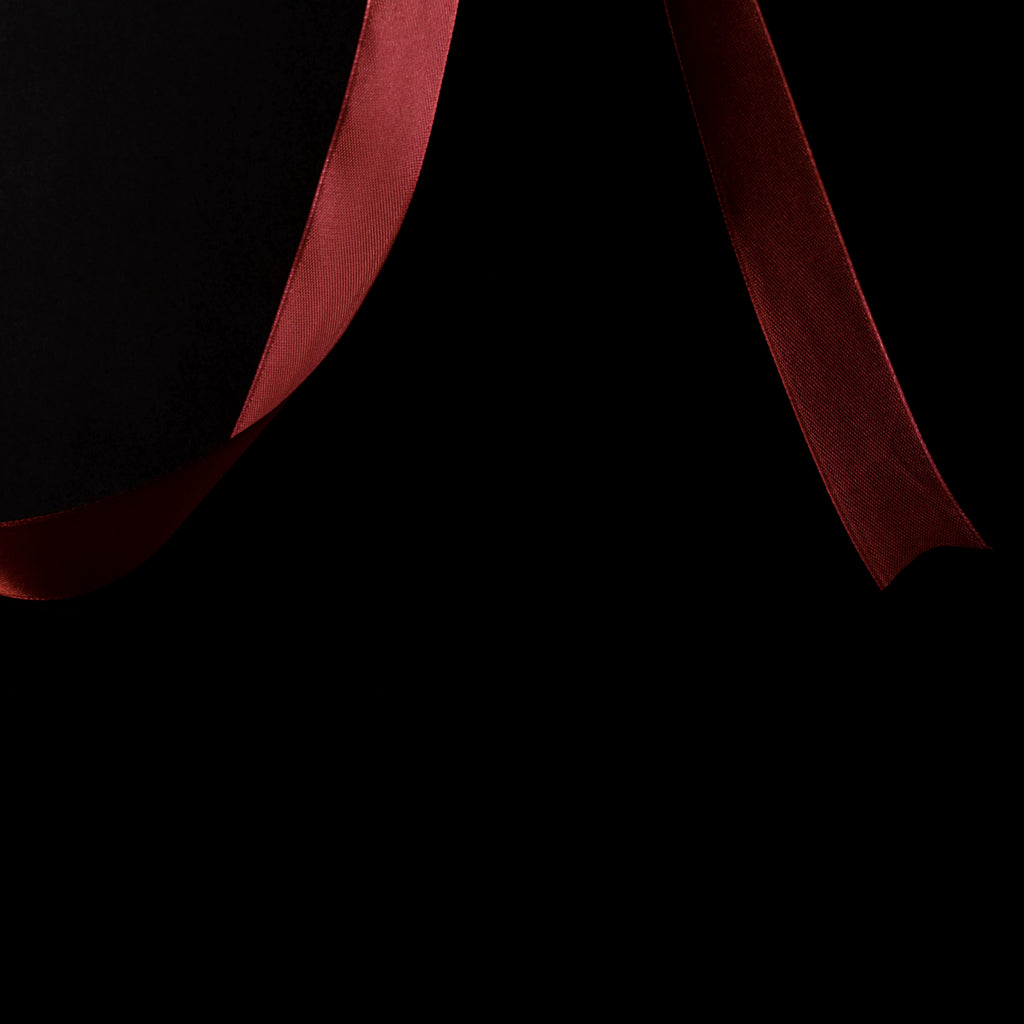 A close-up of a dark red satin book ribbon flowing against a solid black background.